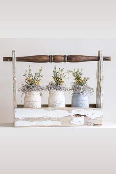 three white vases with plants in them sitting on a wooden shelf next to a stick