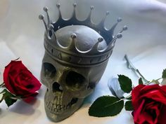 a skull wearing a crown next to two roses on a white surface with one red rose in the foreground