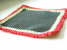 a crocheted dishcloth is sitting on a white counter top with red and green trim