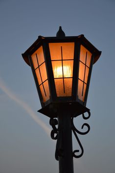 a street light with the sun setting in the sky behind it on a clear day