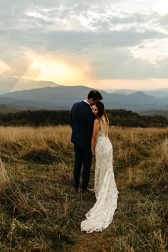 a bride and groom standing in a field at sunset with mountains in the background on their wedding day