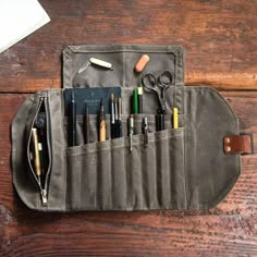 a pencil case with pens, scissors and other items in it on a wooden table