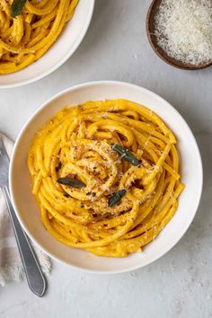 two white bowls filled with spaghetti and topped with parmesan cheese