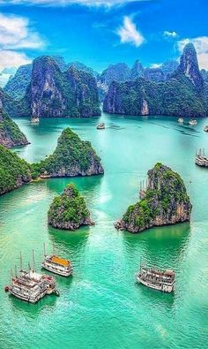 many small boats floating in the water near some rocks and mountains with green trees on them