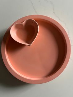 a pink heart shaped dish on a white counter top with a spoon in the shape of a heart