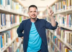 a man standing in front of a book shelf holding his hand up to the camera