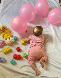 a baby laying on top of a bed next to pink balloons and other toys in front of it