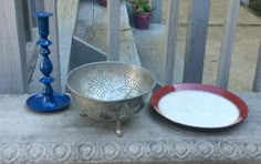 a metal bowl sitting on top of a cement bench next to a blue candle holder