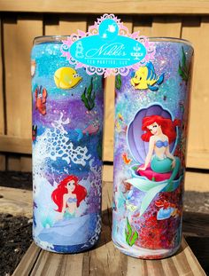 two disney princess tins sitting next to each other on a wooden table in front of a fence