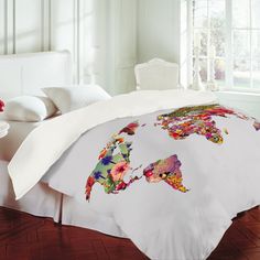 a bed with a white comforter covered in colorful world map artwork on the cover