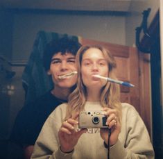 two people taking a selfie in front of a mirror with toothbrushes sticking out of their mouths