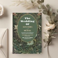 a wedding card on top of a table next to some flowers and greenery in front of it