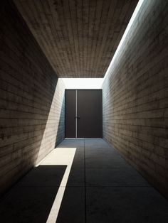 an empty hallway with light coming in from the ceiling and shadows on the wall behind it