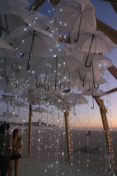 people are standing under umbrellas with lights hanging from them in the rain at dusk