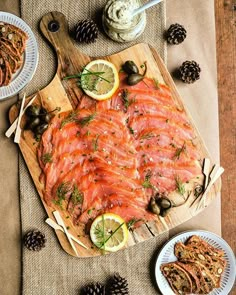 a wooden cutting board topped with sliced up salmon next to olives and pine cones