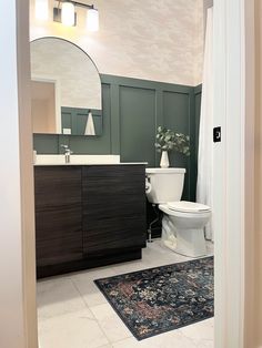 a white toilet sitting next to a sink in a bathroom under a large round mirror