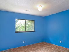 an empty room with blue walls and carpeting on the floor in front of a window