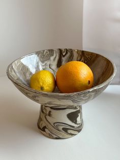 two oranges and one lemon in a marbled bowl on a white countertop