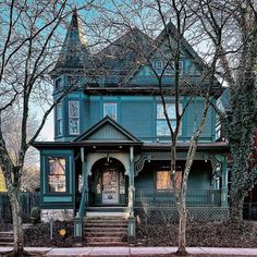 an old victorian house with green trim and blue sidings, surrounded by trees in the front yard