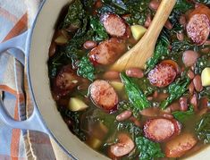 a pot filled with sausage, spinach and potatoes on top of a table next to a wooden spoon