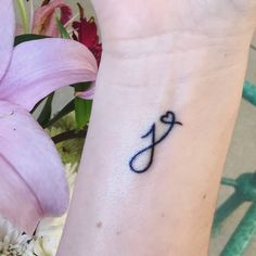 a small tattoo on the wrist of a person with flowers in the back ground and behind her