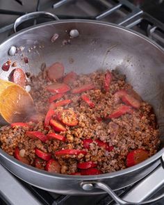 a pan filled with meat and peppers cooking on the stove top next to a wooden spoon