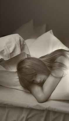 a woman laying on top of a bed under a white comforter with her hair blowing in the wind