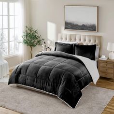 a bed with black and white comforter in a bedroom next to a large window