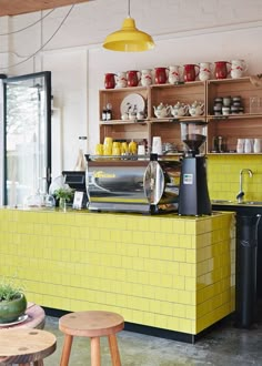 a yellow counter in a restaurant with lots of shelves on the wall and stools around it