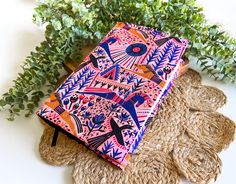 a pink and blue notebook sitting on top of jute coasters next to green plants