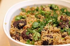 a white bowl filled with rice and meat covered in cilantro, parsley