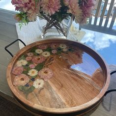 a wooden tray with flowers in it on a table next to a vase filled with pink and white flowers