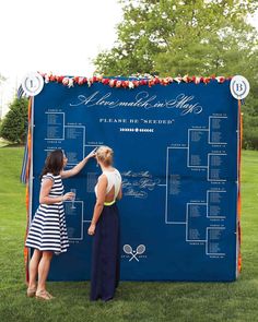 two women standing in front of a blue wall with a tennis tournament bracket on it