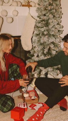 a man and woman sitting on the floor next to a christmas tree with presents in front of them