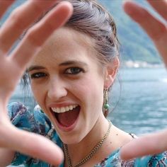 a woman is making the vulcan sign with her hands while standing in front of a body of water