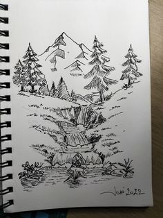 a notebook with a drawing of trees and a waterfall in the middle, on top of a wooden table