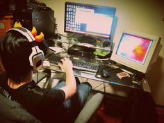 a person sitting in front of a computer with headphones on, and two monitors behind them