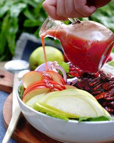 someone pouring dressing into a salad in a bowl with apples, onions and celery