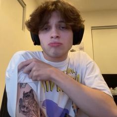 a young man wearing headphones while sitting in front of a computer desk with a tattoo on his arm