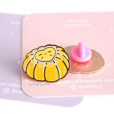 a yellow pin with a pink cupcake on it's back and a small button in the middle