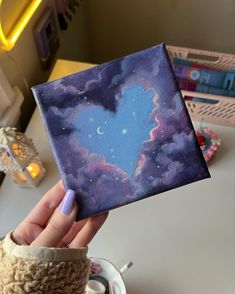 a person holding up a small painting in their hand with the sky and stars painted on it