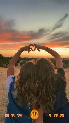 two girls making a heart shape with their hands at sunset in the middle of nowhere