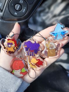 a person holding several cartoon keychains in their hand with a car steering wheel behind them