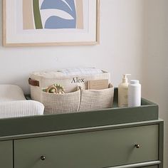 a green dresser with baskets on top and towels in the bottom drawer next to it