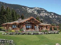 a log cabin style home in the middle of a field with mountains in the background