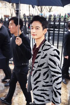 a man holding an umbrella while standing next to other men in black and white outfits