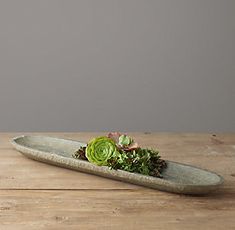 a succulent plant sits on top of a stone boat shaped dish that is sitting on a wooden table