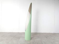 a tall green vase sitting on top of a cement floor next to a white wall