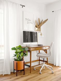 a desk with a computer on it next to a potted plant in front of a window