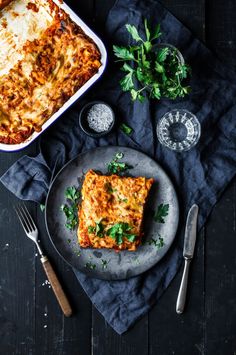 lasagna casserole on a plate with parsley and silverware next to it